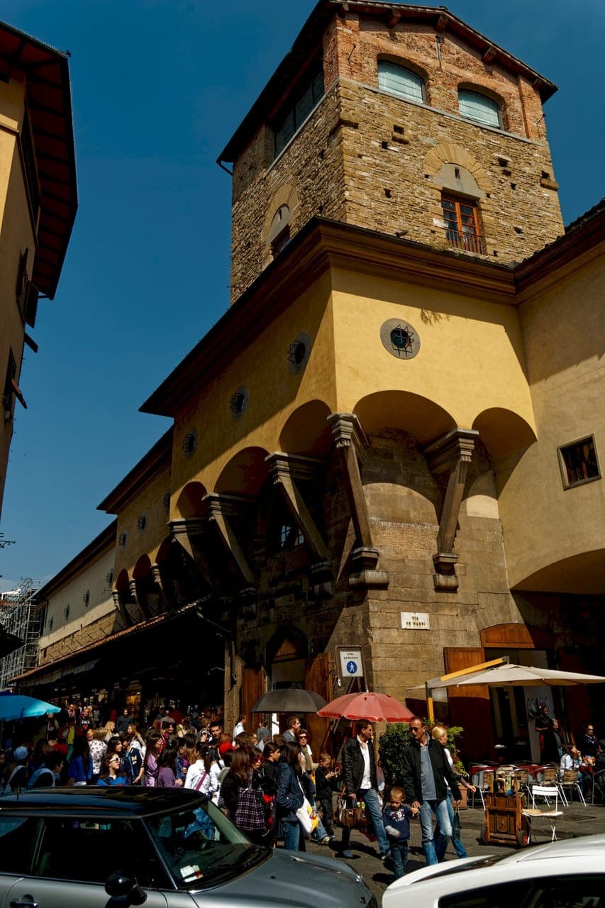 The Vasari Corridor arching past the Torre dei Mannelli at the Ponte Vecchio entrance, running above the shops