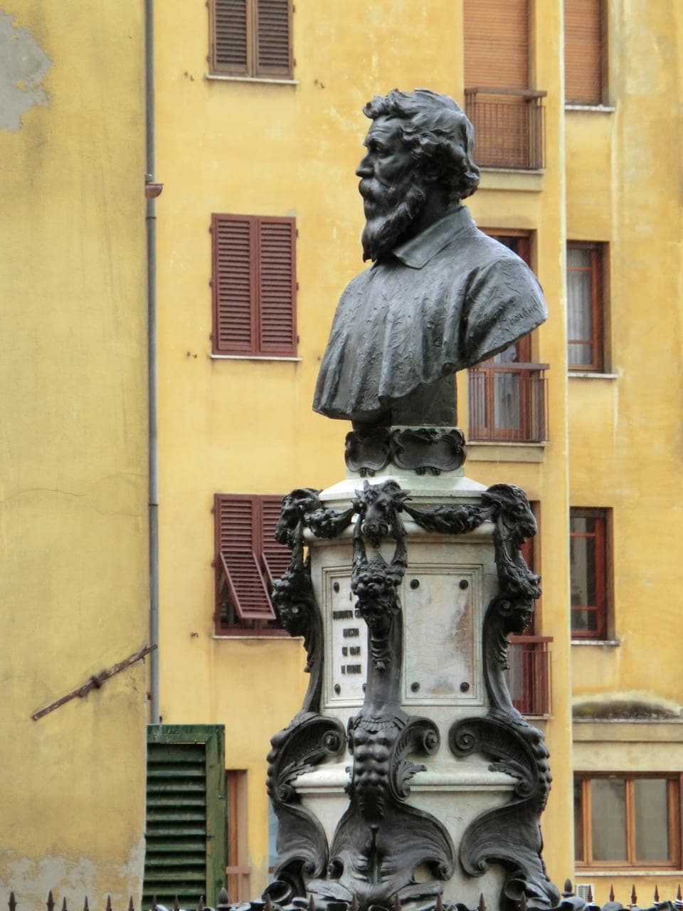 The bronze bust monument of Benvenuto Cellini at the centre of the Ponte Vecchio, on its pedestal by the open-air arches