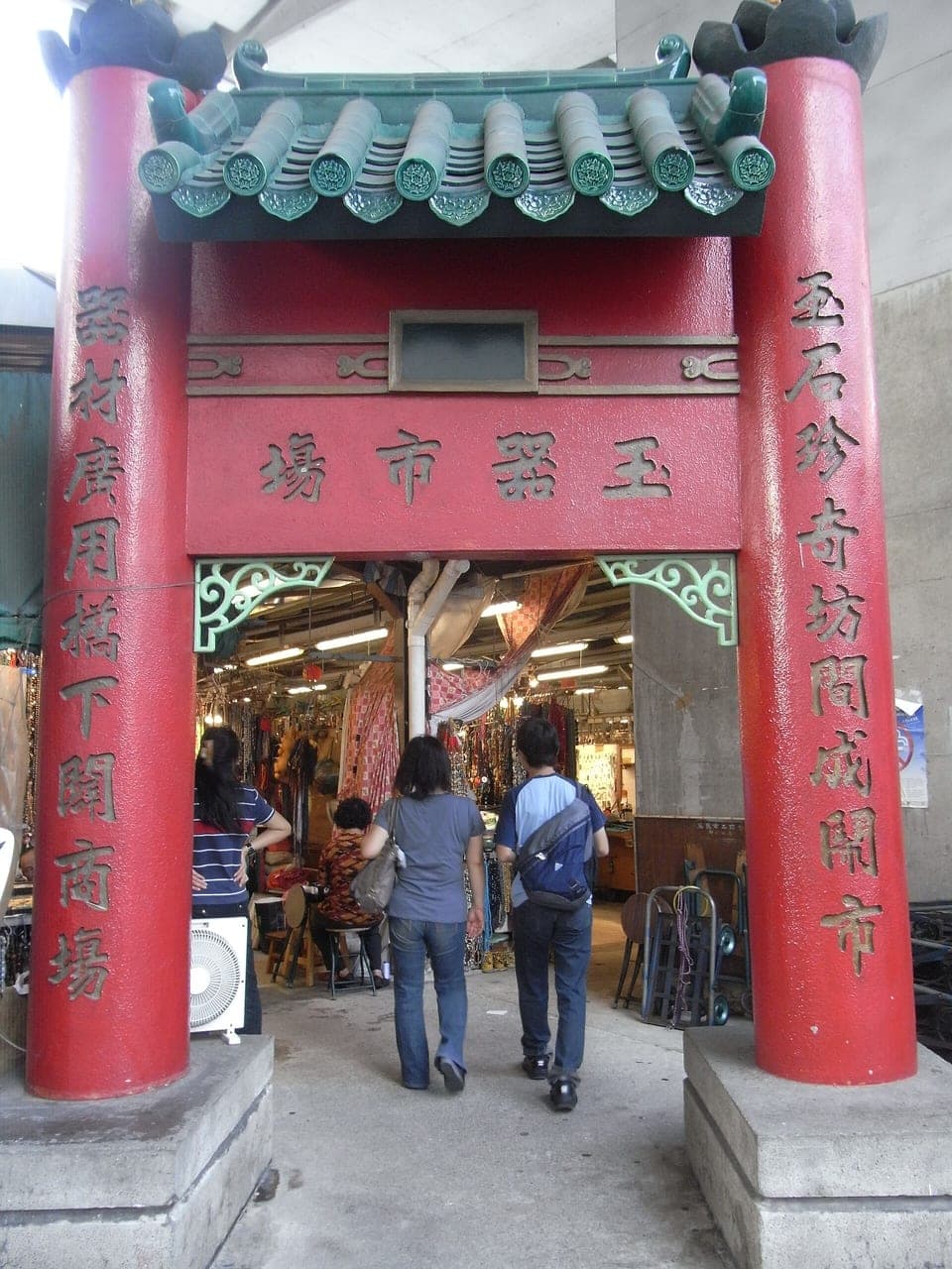 The red ceremonial entrance gate of the Yau Ma Tei Jade Market (玉器市場), with shoppers entering and stalls visible inside
