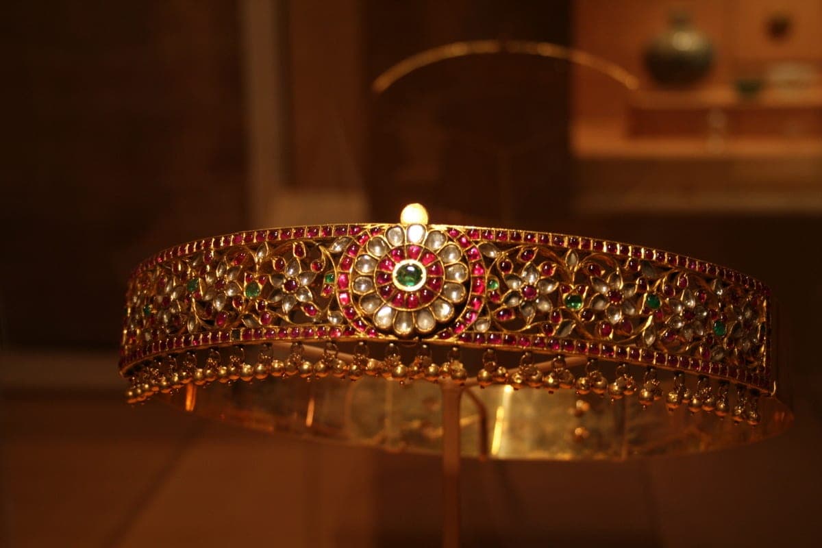 Gold ornament with kundan-style gem setting — gemstones (emerald, rubies) set in floral patterns of pure gold foil, with pearls