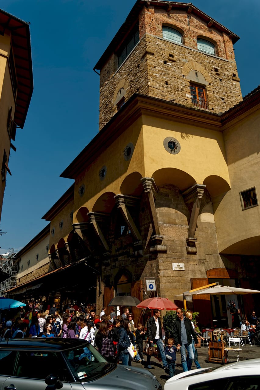 The Vasari Corridor arching past the Torre dei Mannelli at the Ponte Vecchio entrance, running above the shops